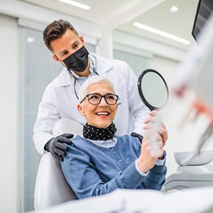 Senior female dental patient holding hand mirror, admiring her teeth