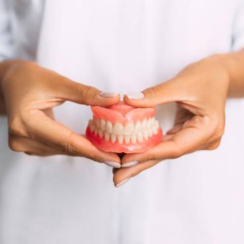 Manicured hands holding full set of dentures