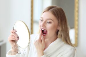 Woman in bathroom, examining her teeth in mirror